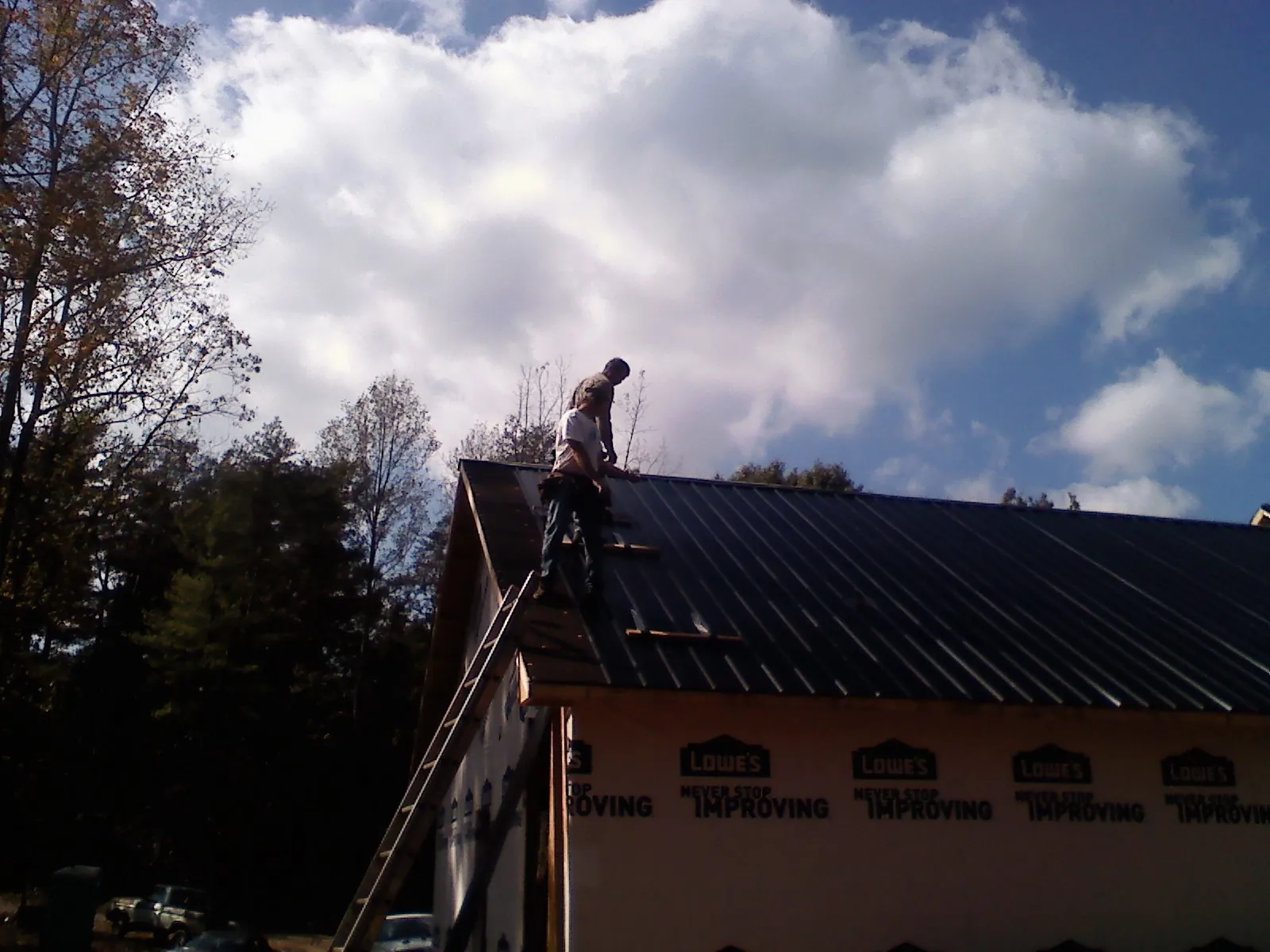 Roofer fastening dark metal panels high against a cloudy sky, from a Roof Inspection job in Orange